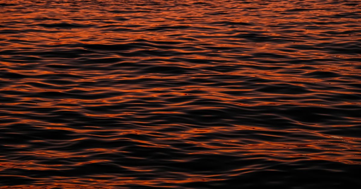 Capture of beautiful red hues reflecting on gentle waves during sunset.